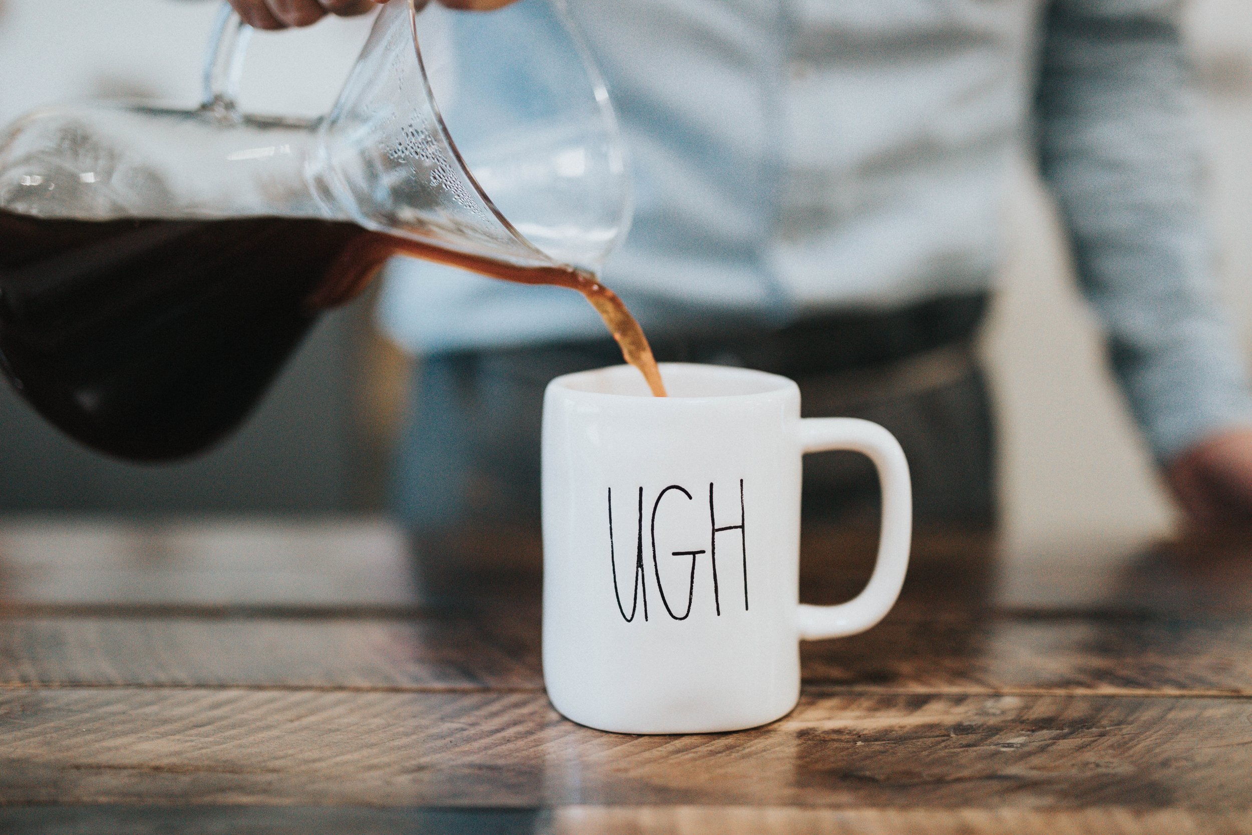 Sharply dressed man pours coffee into white mug that reads "UGH" in capital letters